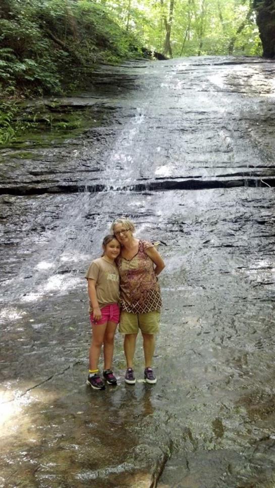Two friends pose happily by a cascading waterfall, surrounded by lush greenery in nature.