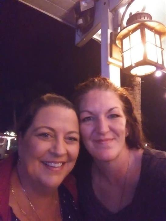 Two friends smile near a warm lantern, enjoying a relaxed night atmosphere.