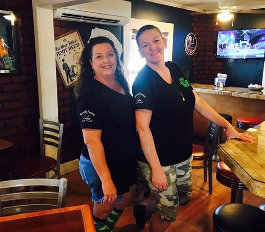 Two bartenders smile and pose in a vibrant pub, showcasing their teamwork and camaraderie.