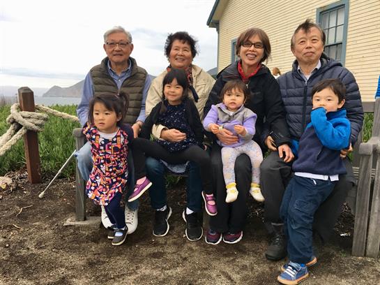 Multiple generations of a family pose together on a bench, enjoying a moment outdoors in nature.