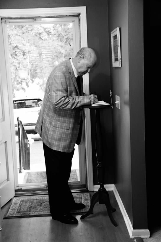 An elderly man is engaged in writing notes by the entrance of his warm and inviting home.