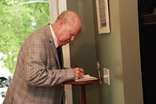 Senior gentleman takes notes at a small table in a quiet, well-lit room.