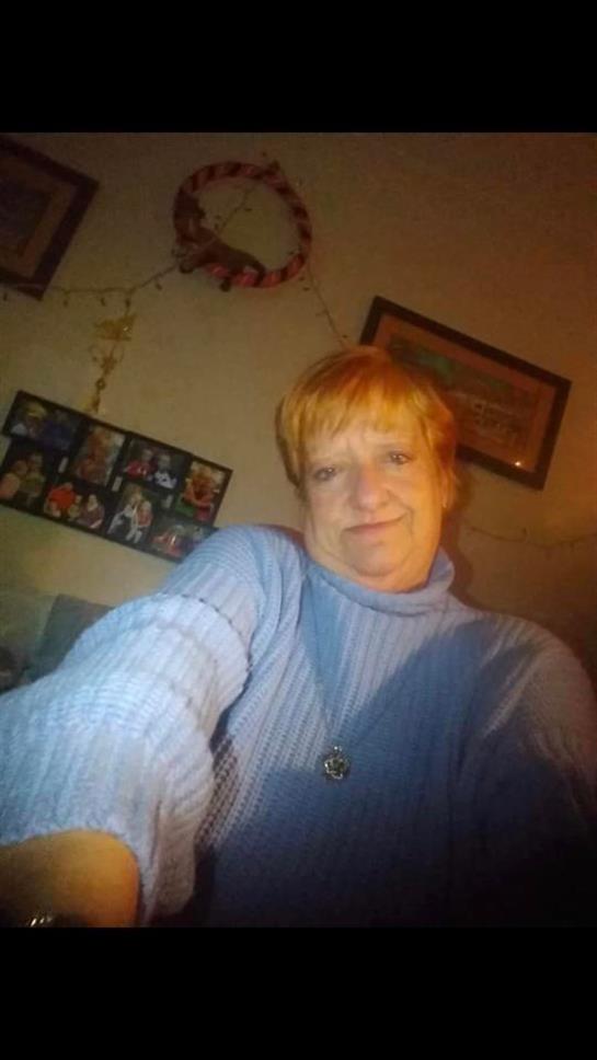 A woman with short, bright hair smiles while taking a casual selfie in her home.