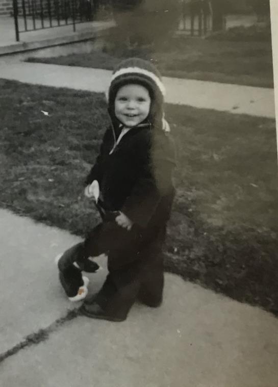 A young child smiles while holding a toy, enjoying playtime outdoors on a warm day.