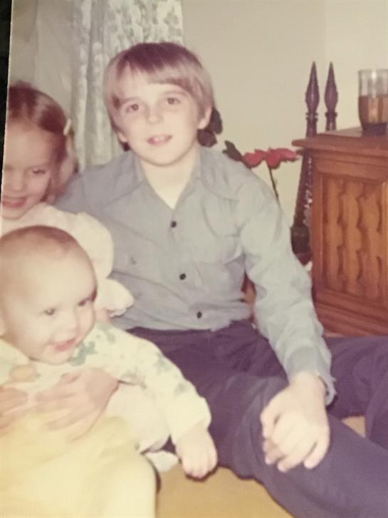 Three children gather around a baby in a warm and inviting living room filled with nostalgia.