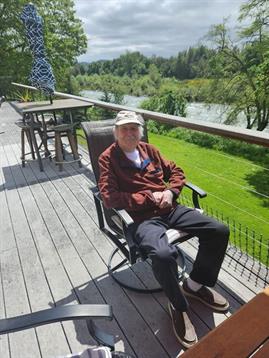 Elderly man enjoys a tranquil moment in a rocker on a wooden deck surrounded by nature.