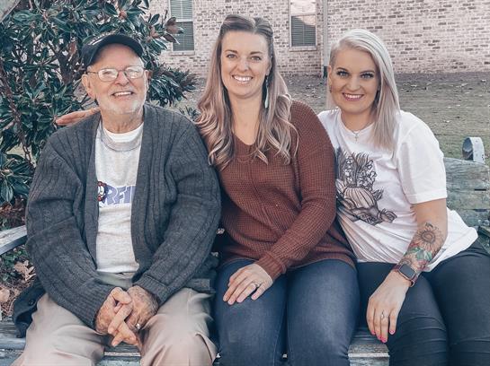 Three family members enjoy a moment of joy while sitting on a bench outside in their garden.