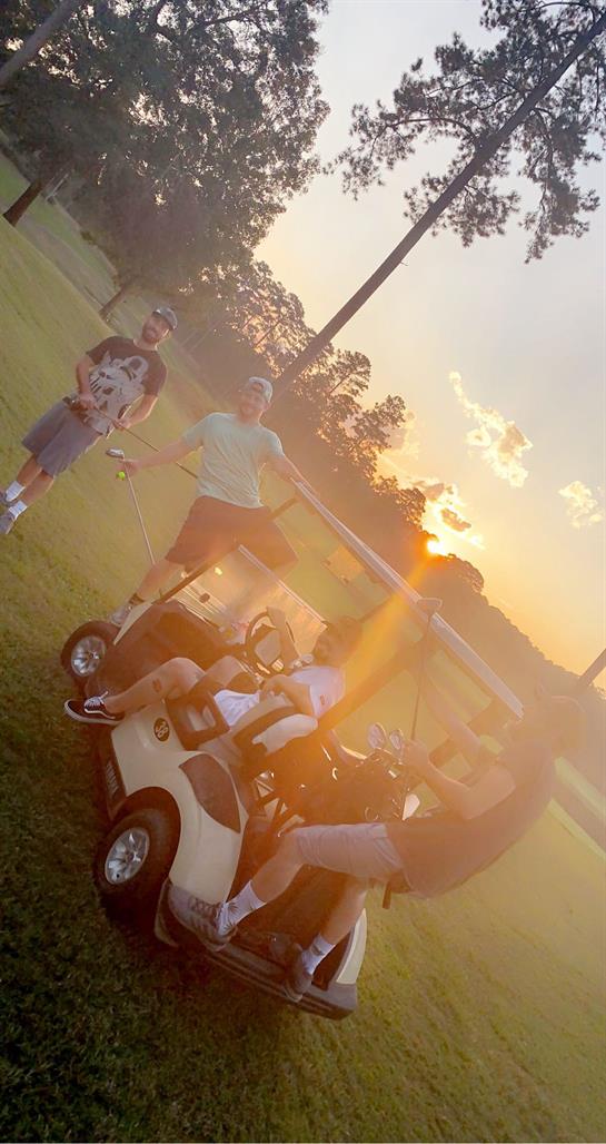Group of friends gather around a golf cart enjoying a sunset, sharing laughter and drinks.