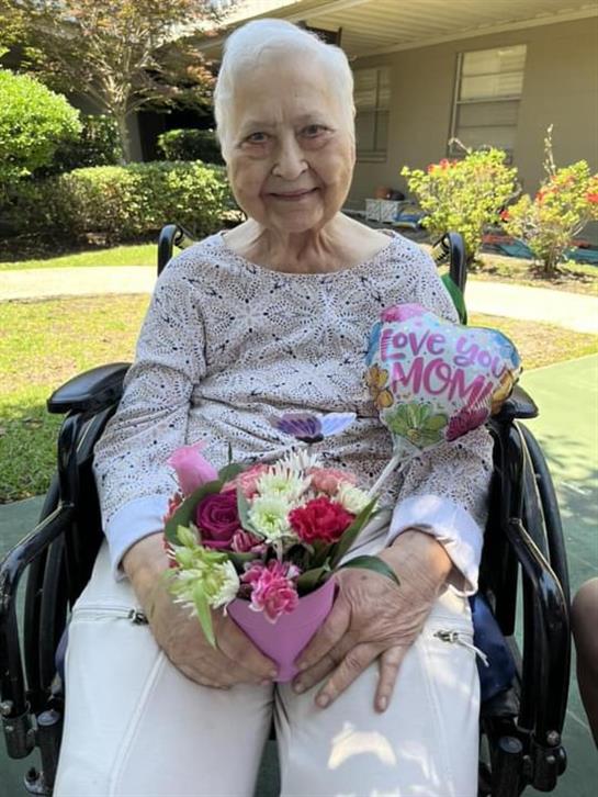 An old woman in a wheelchair holding flowers and a balloon