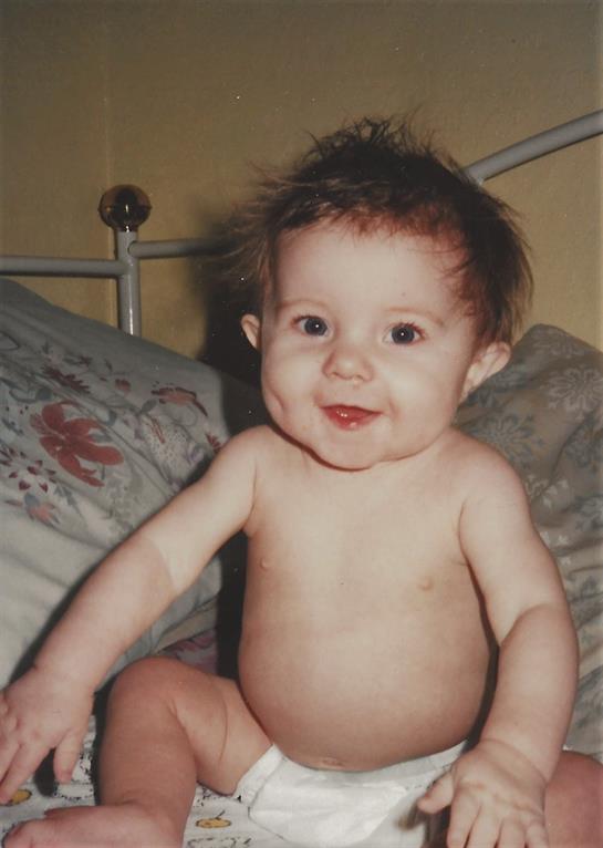 Baby with a joyful smile sitting on a bed in a soft and inviting room setting.