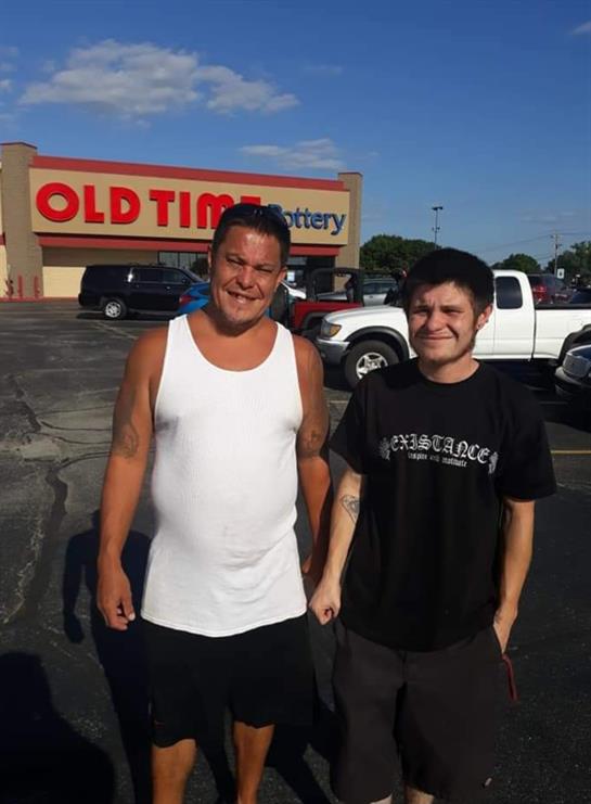 Two men happily enjoy their time outside the Old Time Lottery store in daylight.
