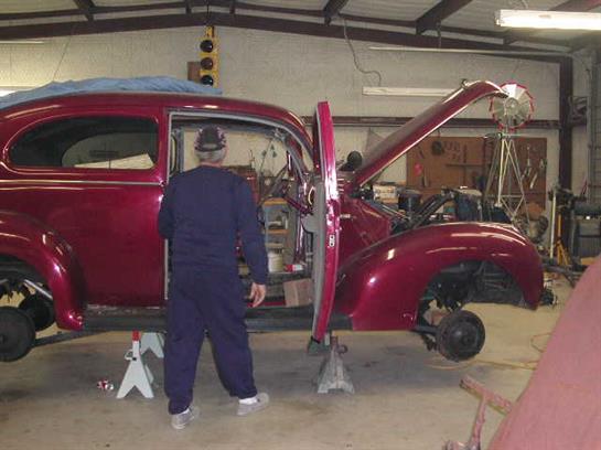 A worker inspects a classic car's exposed engine during its restoration in a workshop.