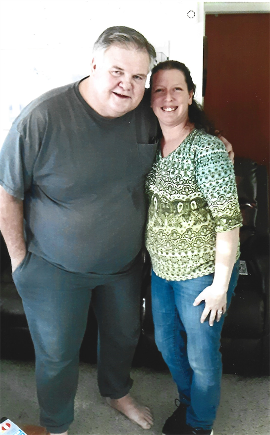 Two people stand side by side smiling warmly, enjoying a friendly moment in a cozy living room.