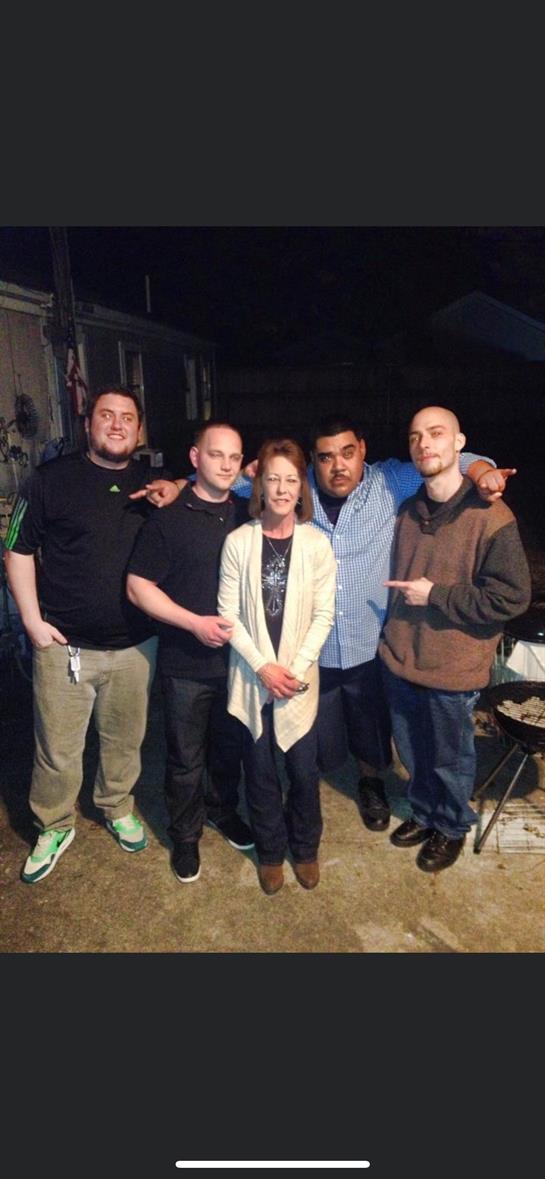 Five friends smile and gather around, enjoying a casual evening together outdoors while socializing.