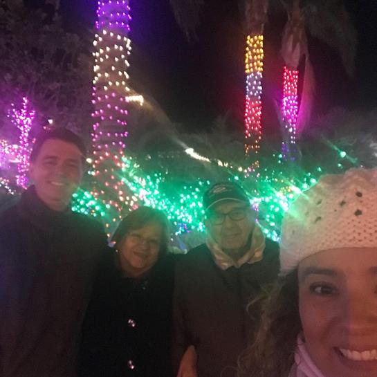 Group of four friends enjoy a festive atmosphere surrounded by brightly lit trees at night.
