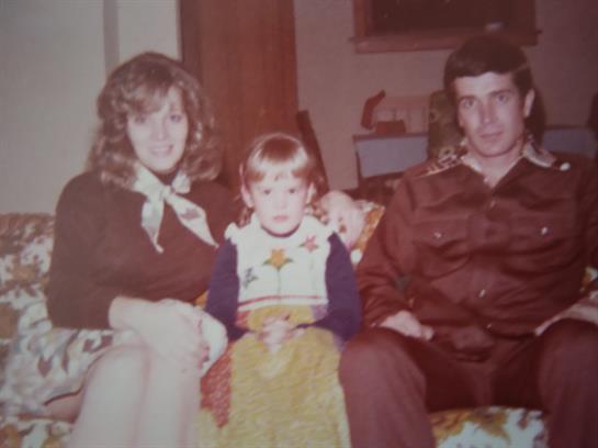 Three individuals pose for a loving family portrait in a warm living room setting.