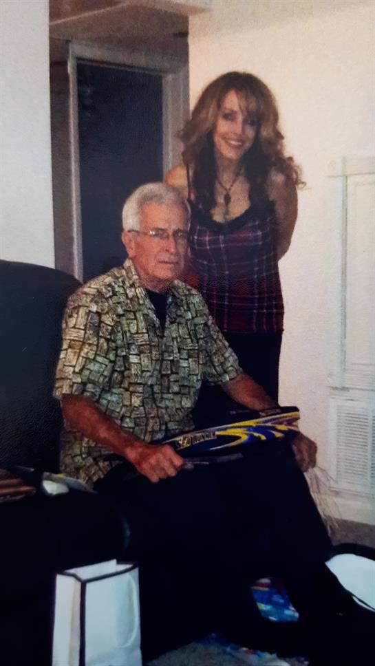 A man in a patterned shirt holds a baseball bat while a woman stands behind him, smiling.