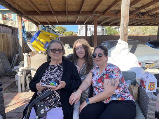Three women relax together in a backyard, sharing smiles and laughter on a sunny afternoon.