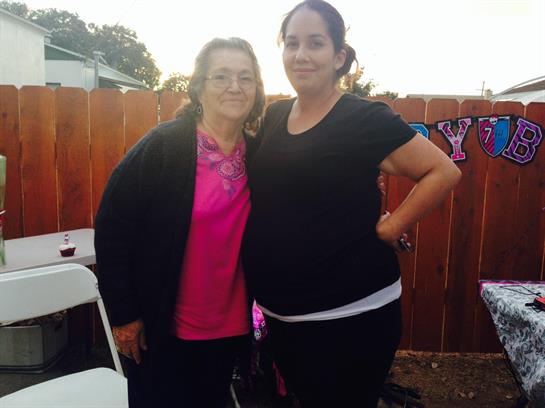 Two women stand together smiling during a family event in a cozy backyard at sunset.