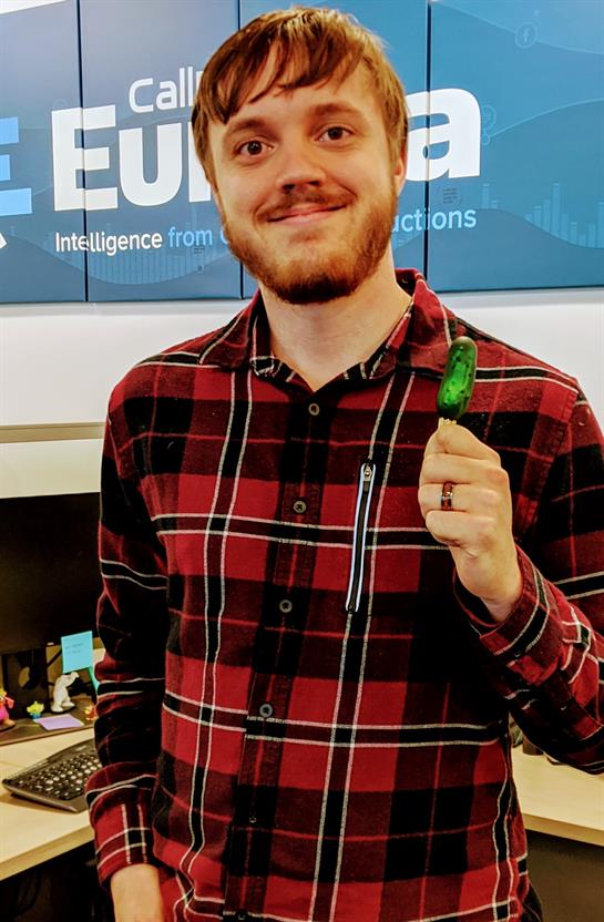 Someone is smiling while standing in an office, showcasing a green item in hand.