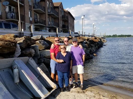 Four family members smile together at the riverbank, enjoying a sunny afternoon near their homes.