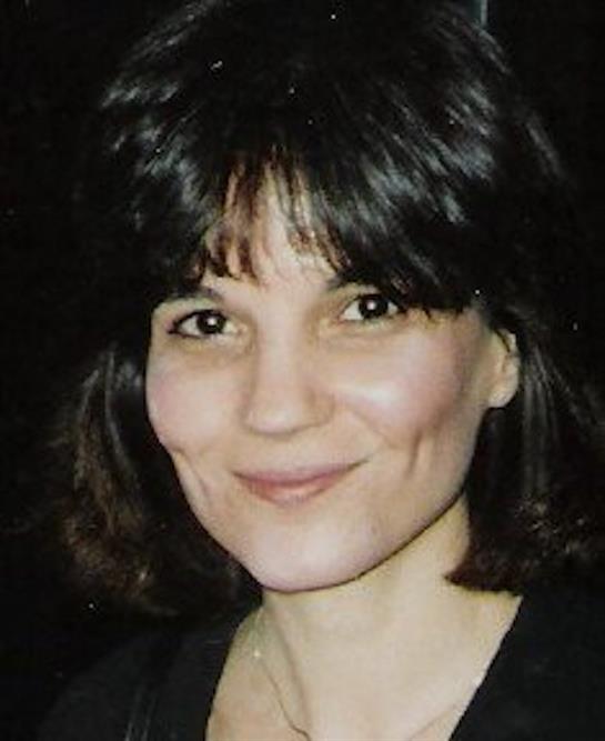 A woman with dark hair smiles warmly, showcasing her friendly demeanor and beautiful features.