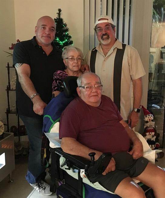 Family members celebrate together with an elderly man in a wheelchair, decorated room.