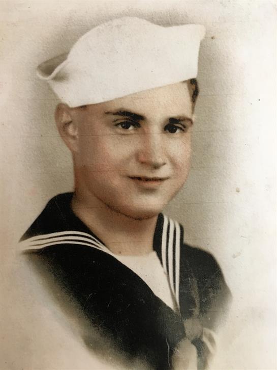 A young sailor in formal uniform smiles softly, showcasing pride and youthfulness in his demeanor.