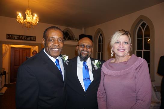 Three friends gather in formal attire, celebrating together with smiles at a festive evening event.