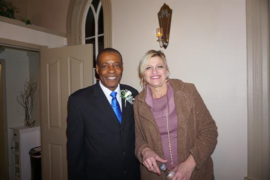 Two individuals stand close together, smiling happily at a formal gathering in an elegant setting.