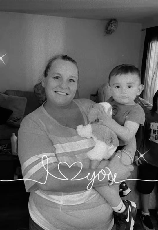 A joyful woman embraces a young child with a stuffed animal in a warm home environment.