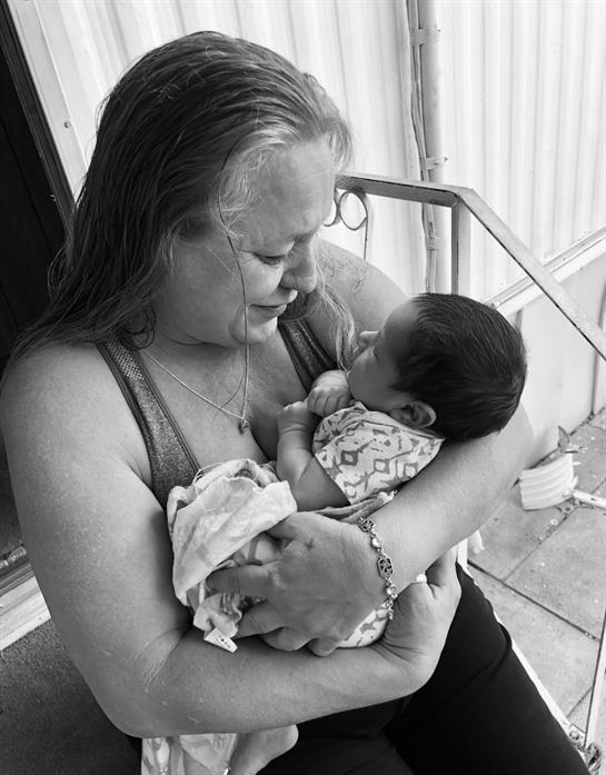 Grandmother joyfully cradles her newborn grandchild on the porch, sharing a loving gaze.