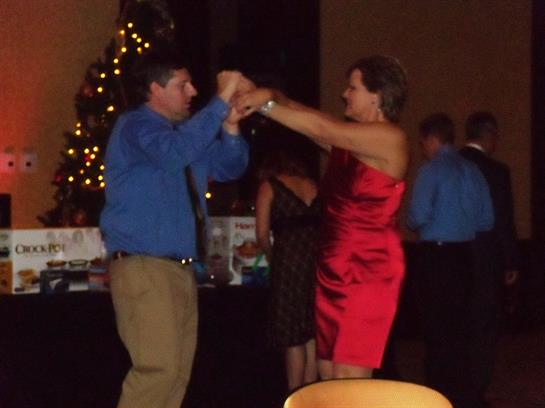 Two individuals dance together amid festive decorations and warm lights at a holiday gathering.