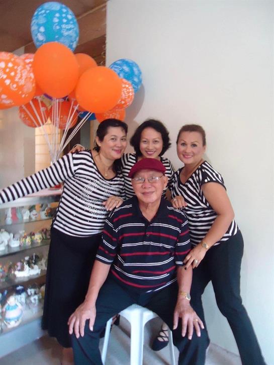 Four people smile and pose at a festive gathering with orange and blue balloons.