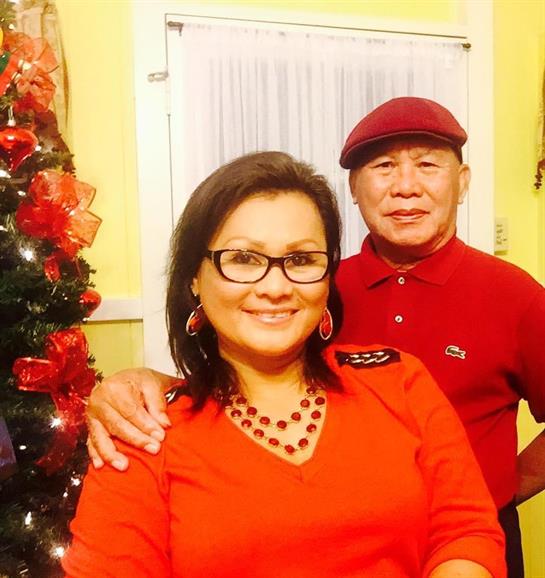 A woman in red and a man in matching attire pose happily beside a decorated Christmas tree.