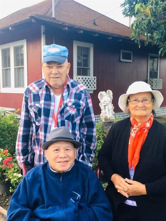 Three elderly individuals enjoy time together in a vibrant garden on a warm day.