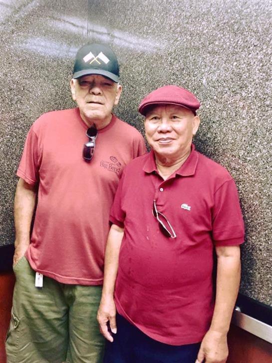 Elderly men wear similar red apparel while smiling in an elevator during the daytime.