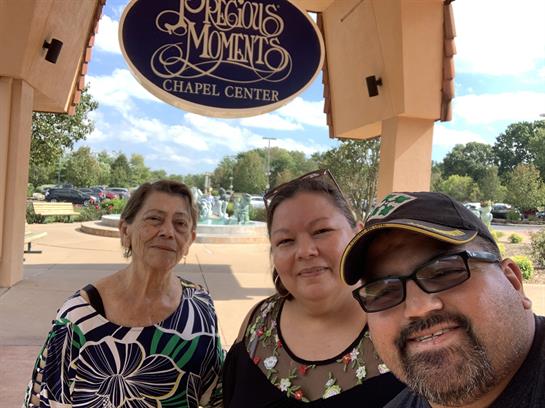 Three individuals smile at the camera in front of a chapel center, enjoying a bright day outdoors.