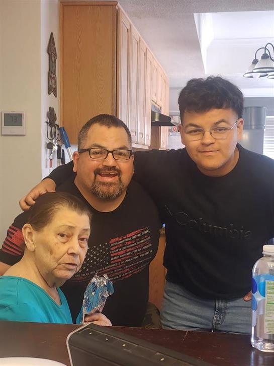 A woman, a man, and a young man happily pose together in a kitchen.