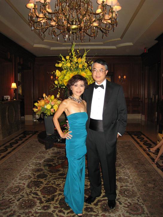 A well-dressed couple stands together at a formal event surrounded by vibrant floral decorations.