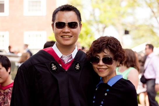 Two graduates don caps and gowns while enjoying a cheerful outdoor celebration with family.