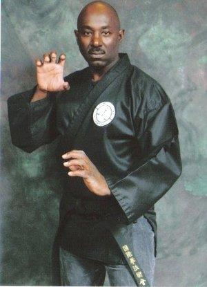 A martial arts expert poses in a traditional black uniform, showcasing his skills and technique.