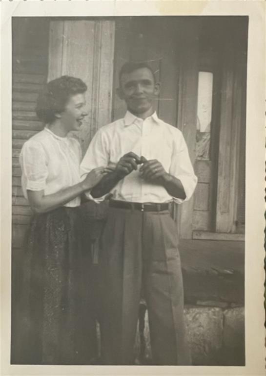 Two smiling individuals enjoy a lighthearted moment on a wooden porch in the summertime.
