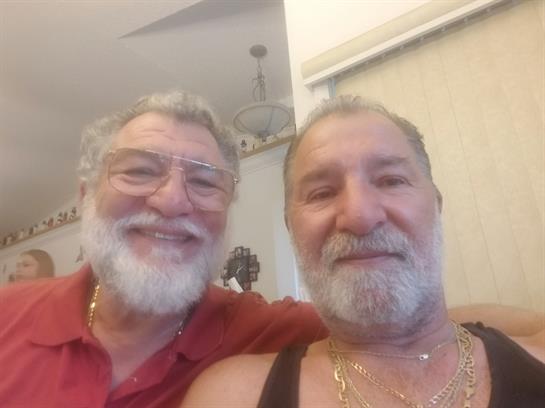 Two joyful older men with beards share smiles and laughter in a relaxed indoor setting.
