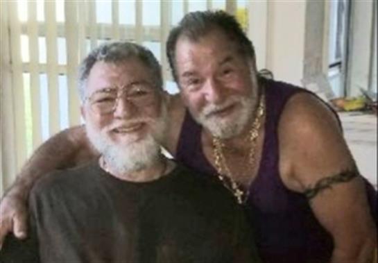 Two men with facial hair smile warmly, enjoying time together in a relaxed atmosphere.