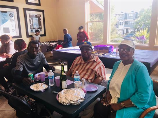 People gather around tables sharing food and drinks in a lively community center setting.