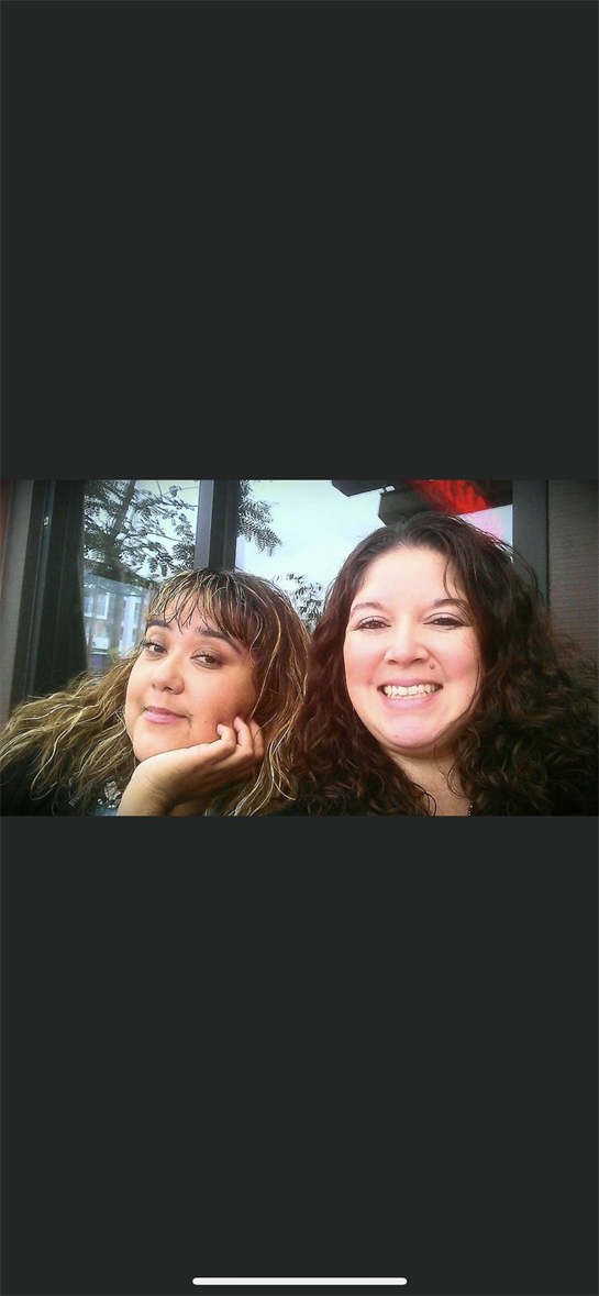 Two friends pose for a cheerful selfie, relaxing outside a cafe with natural light.