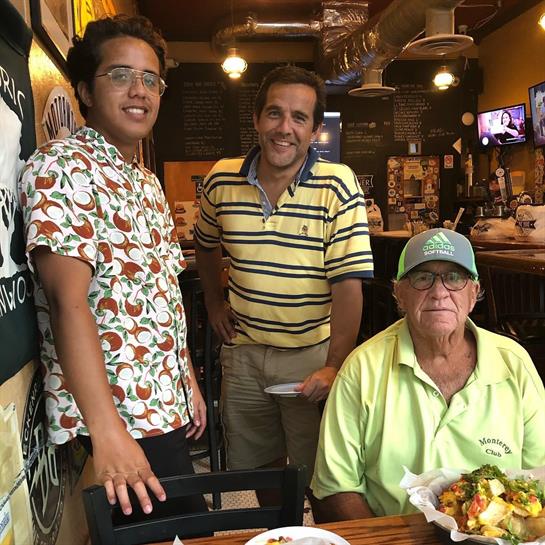 Three friends smiling together at a cozy restaurant while enjoying delicious food and drinks.