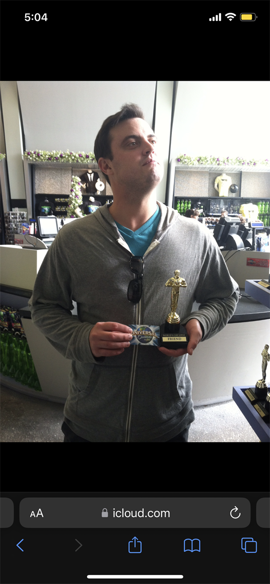 Man holds a trophy and card while posing confidently in a sports retail store setting.
