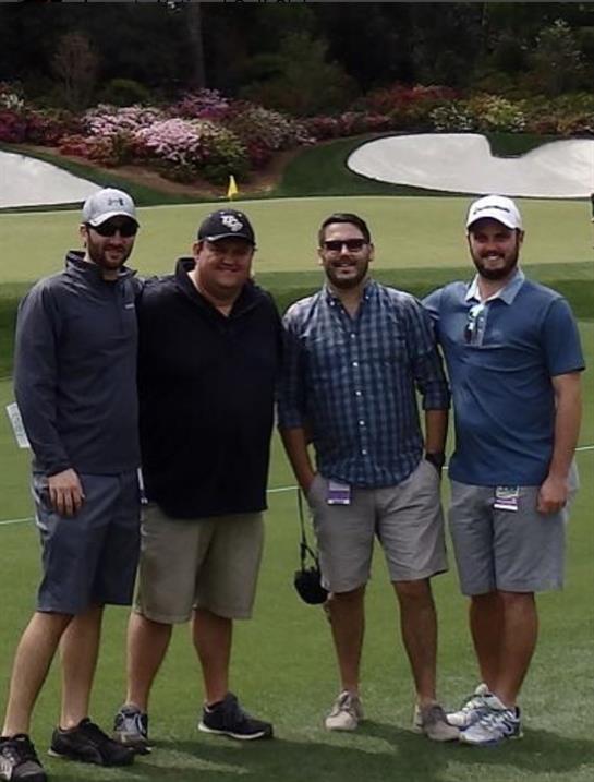 Four friends are posing on a golf course, smiling and enjoying a sunny day together.